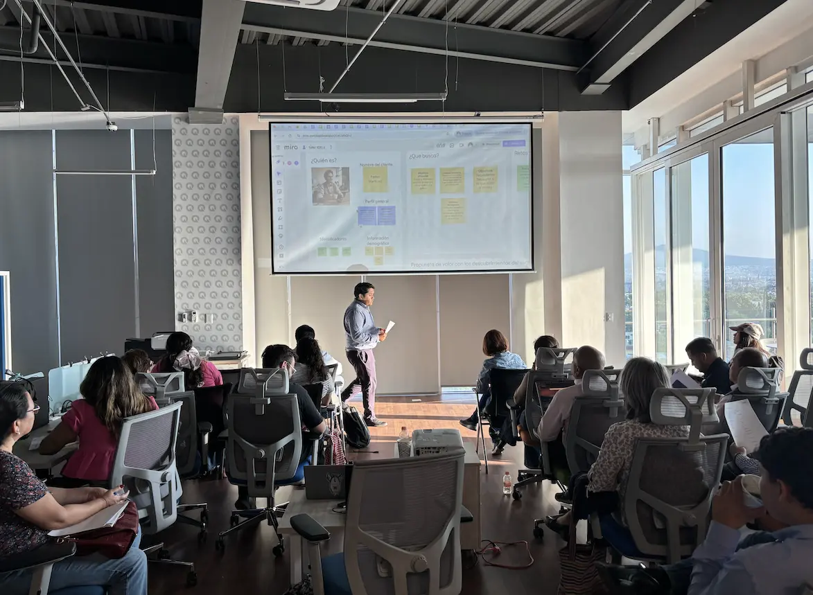 Taller de ventas de RUZC: un grupo de profesionales en una sala con ventanales escucha a Enrique Ruiz Sandoval frente a la pantalla.
